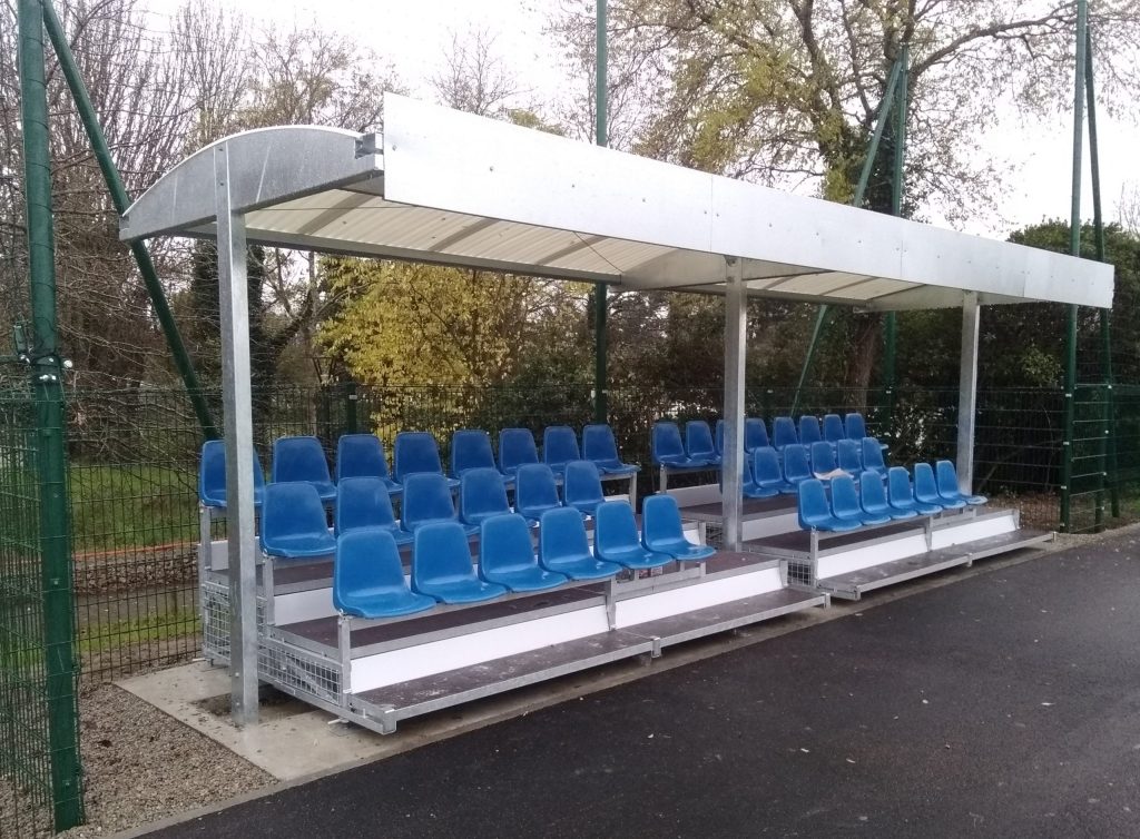 Stadium spectator shelter with blue seats installed at the pitch side