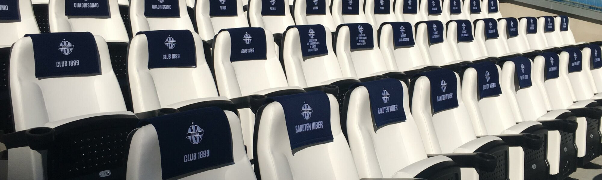 Rangées de fauteuils blancs équipés de têtières bleu marine brodées en tribune couverte