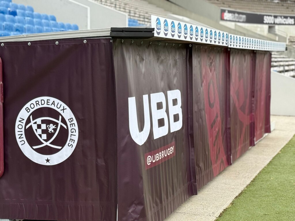 Burgundy fabric with the Union Bordeaux-Bègles logo hung across the front of a dugout