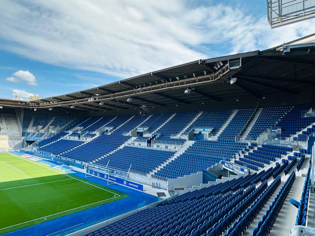 Angled view of a stand at the Stade de la Meinau, rows of blue seats forming a light pattern above the perimeter track